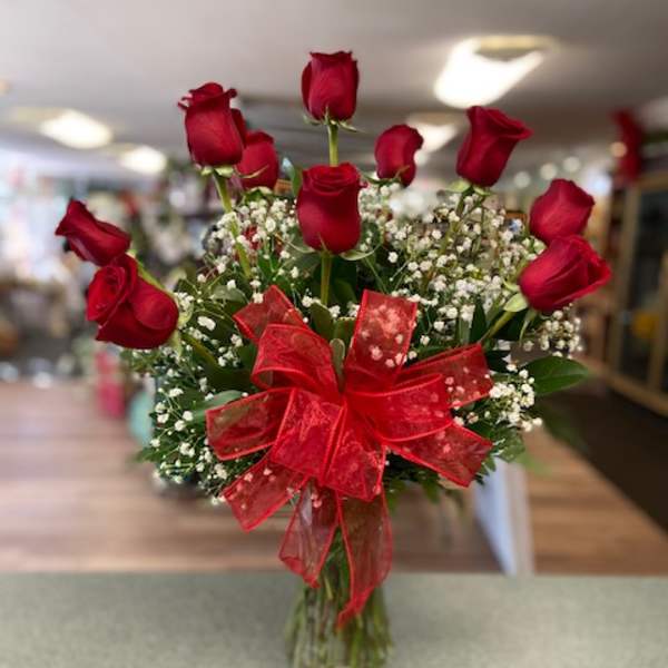 Red roses in a glass vase with baby's breath and a red bow