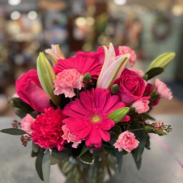 Compact bouquet of bright pink gerbera daisies, roses, carnations, and lilies in a clear glass vase