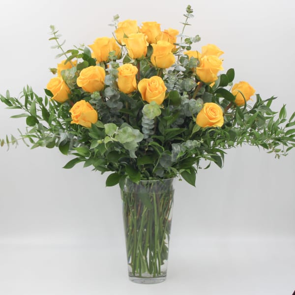 Yellow roses in a clear glass vase with greenery