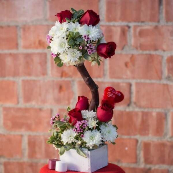 Heart-shaped floral arrangement with red roses and white daisies on a branch stand