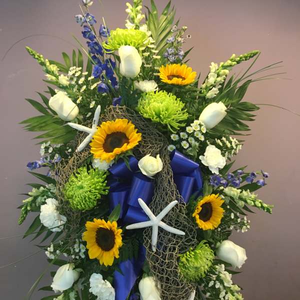 Large floral standing spray with sunflowers, white roses, and blue ribbon