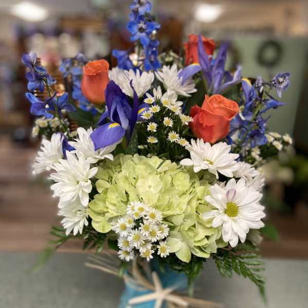 Mixed bouquet with blue, white, and orange flowers in a glass vase