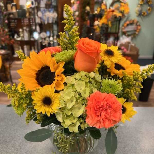 Bright bouquet with sunflowers, orange roses, and carnations in a glass vase