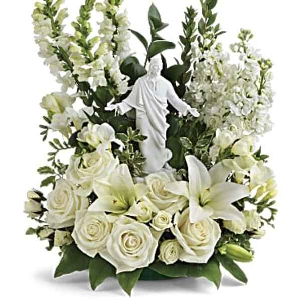White roses and lilies arranged around a small statue in a vase