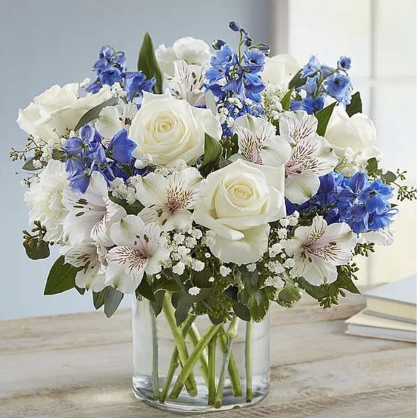White roses and blue flowers arranged in a clear glass vase.