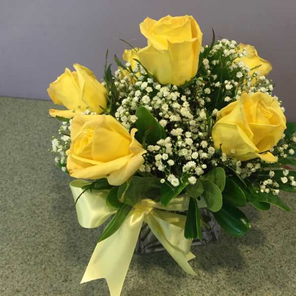 Yellow roses arranged with baby's breath in a glass vase with a ribbon