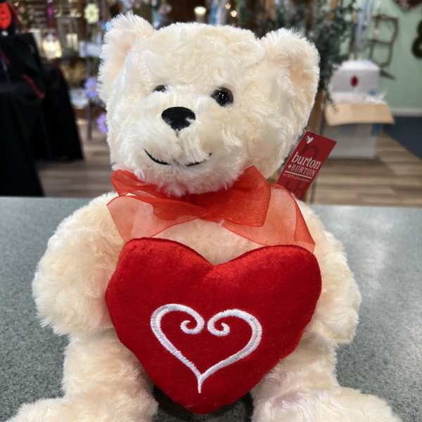White teddy bear holding a red heart and wearing a red ribbon