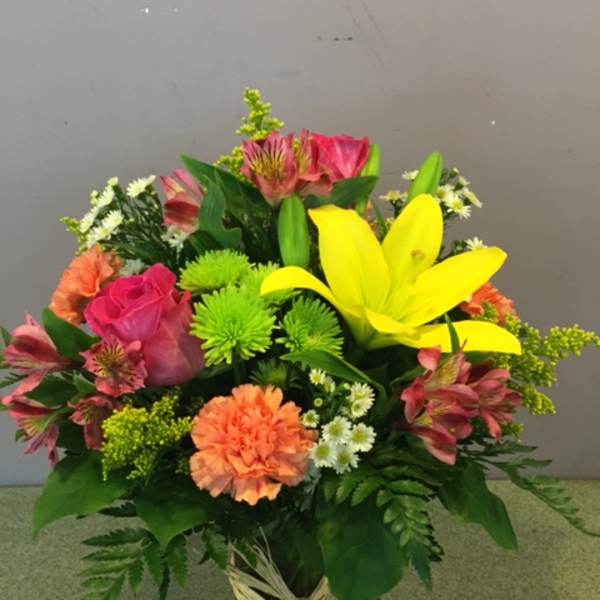 Mixed bouquet with yellow lilies, pink roses, and orange carnations in a glass vase