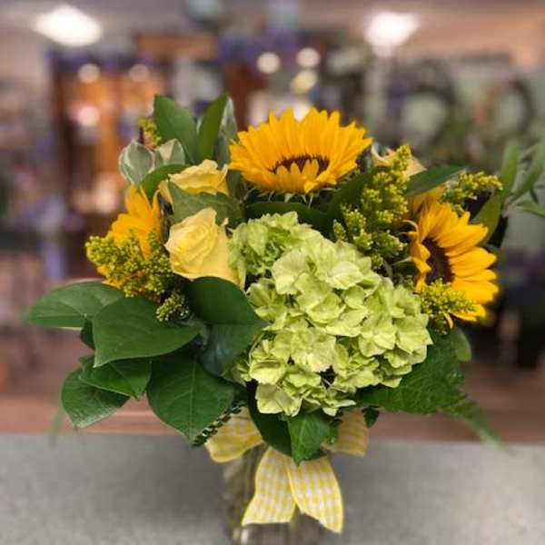 Bouquet of sunflowers, pale green hydrangea, and yellow roses in a glass vase