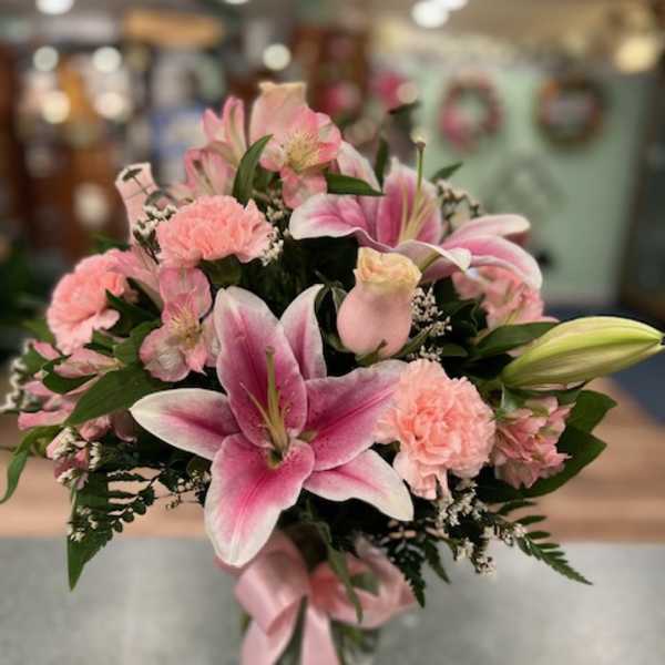 Pink lilies and carnations arranged in a glass vase with a pink ribbon.