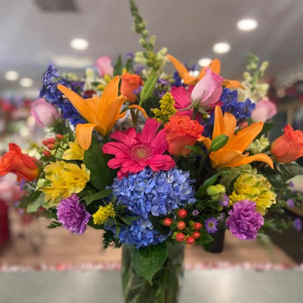 Colorful mixed bouquet in a glass vase with lilies, roses, hydrangeas, and daisies
