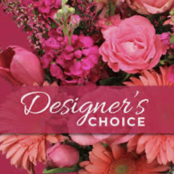 Pink floral arrangement with roses and daisies behind a Designer's Choice label