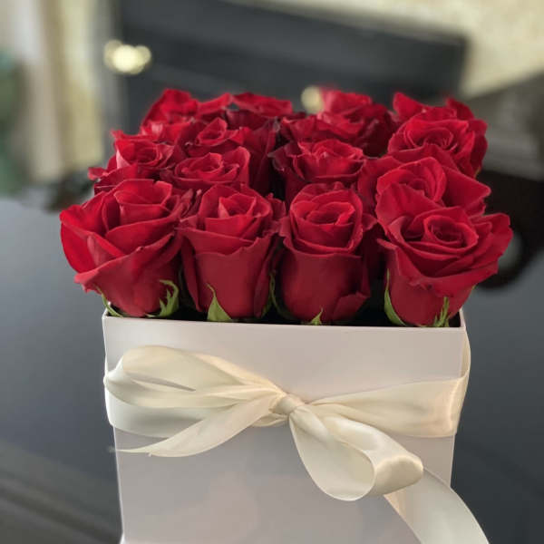 Red roses arranged in a white box tied with a cream ribbon