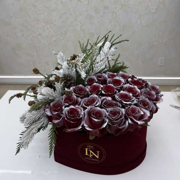 Red roses in a burgundy box with frosted winter greenery and pinecones
