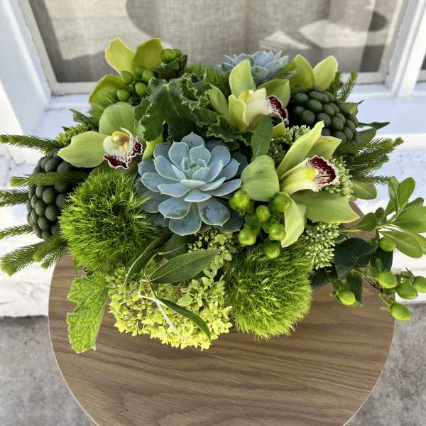 Green floral arrangement with orchids, succulents, and hydrangea on a round table