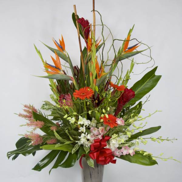 Tall tropical flower arrangement in a silver vase with orange and red blooms