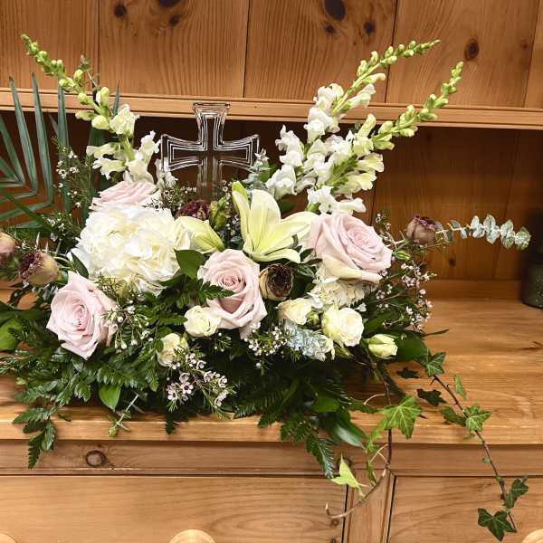 Pastel floral arrangement with roses, lilies, and a cross centerpiece