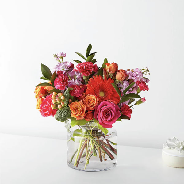 Mixed bouquet of roses, gerbera daisies, and carnations in a clear glass vase