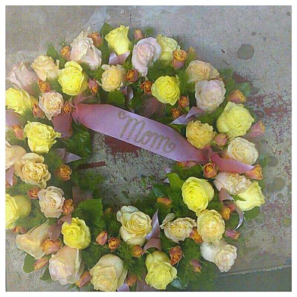 Circular wreath of pale roses with a lavender ribbon reading "Mom"