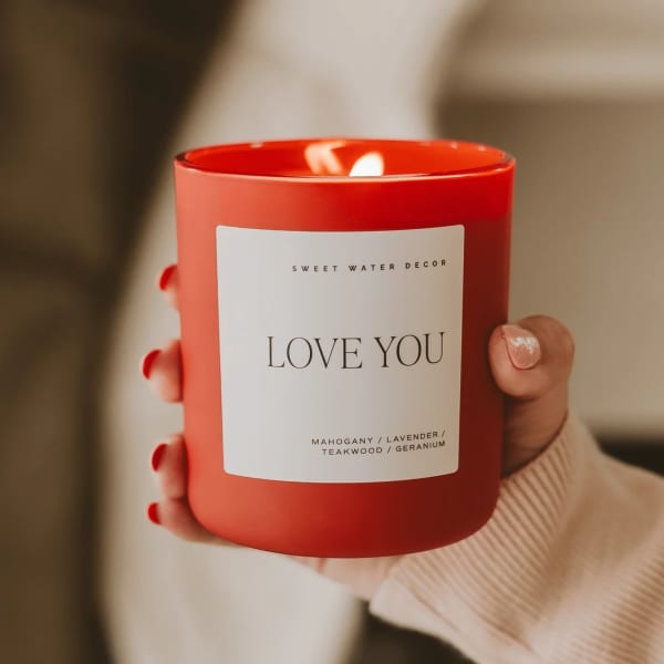 Red candle in a glass jar labeled "LOVE YOU" being held in a hand