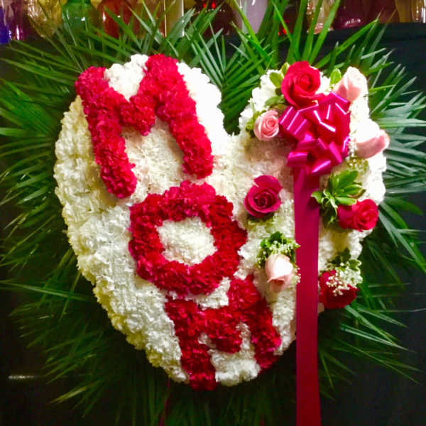 Heart-shaped floral tribute with red and white flowers and a pink ribbon