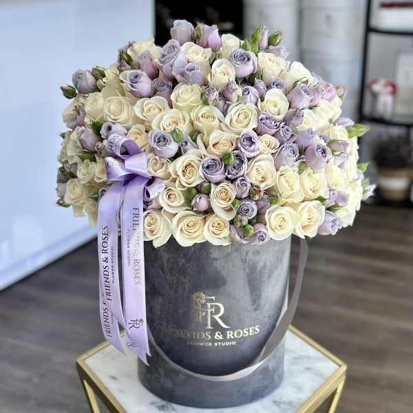 Bouquet of cream and lavender roses in a round hat box with a purple ribbon