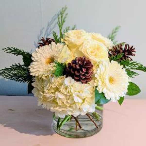 Cream floral arrangement in a clear glass vase with pinecones and greenery