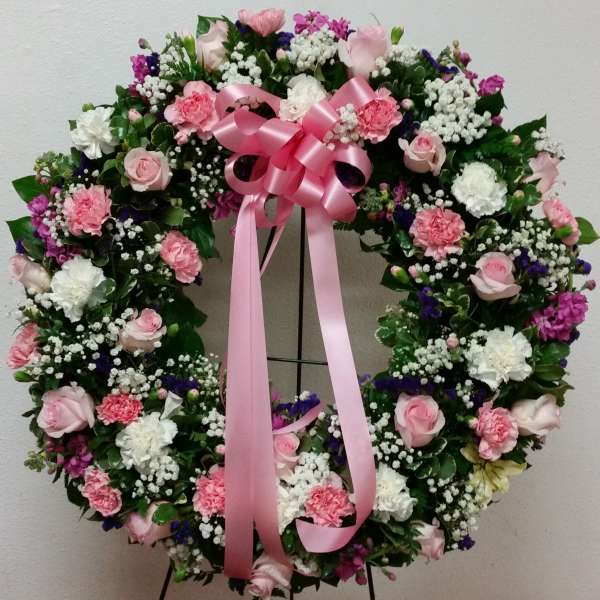 Heart-shaped floral wreath with pink ribbon on a stand