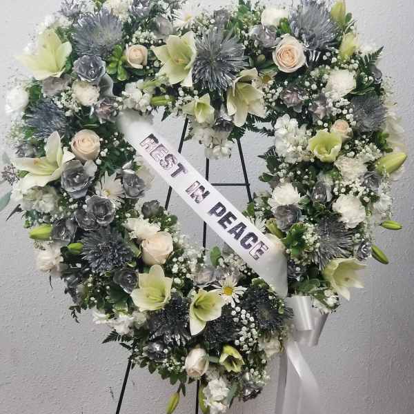 Heart-shaped funeral wreath with white and pale green flowers and a peace ribbon