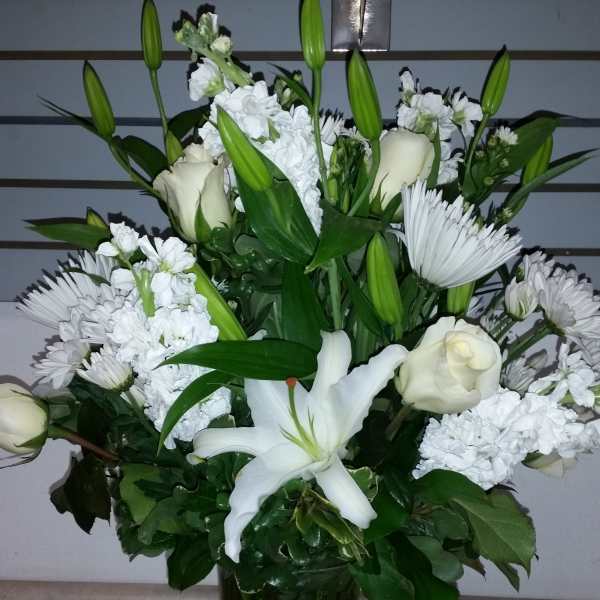 White lilies, roses, and daisies arranged in a tall glass vase