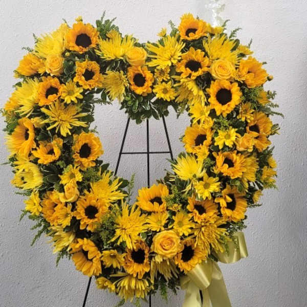 Heart-shaped yellow floral wreath on a stand with a ribbon