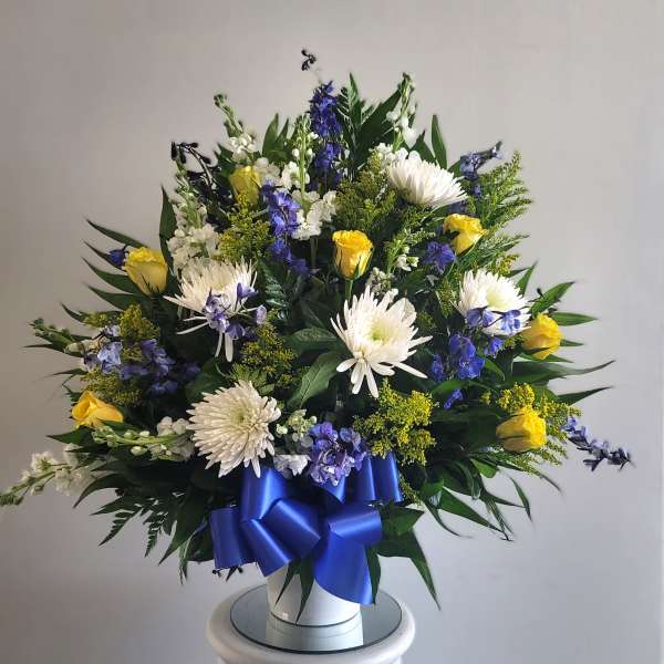 White and yellow floral arrangement with blue ribbon in a white vase