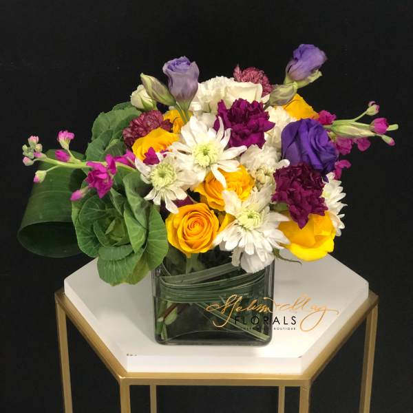 Mixed bouquet of yellow, white, purple, and pink flowers in a glass vase