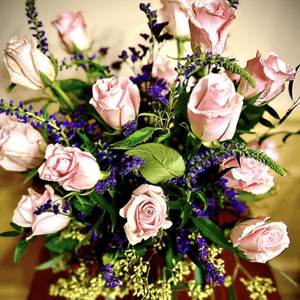 Vase arrangement of light pink roses with purple accent flowers in a clear glass vase