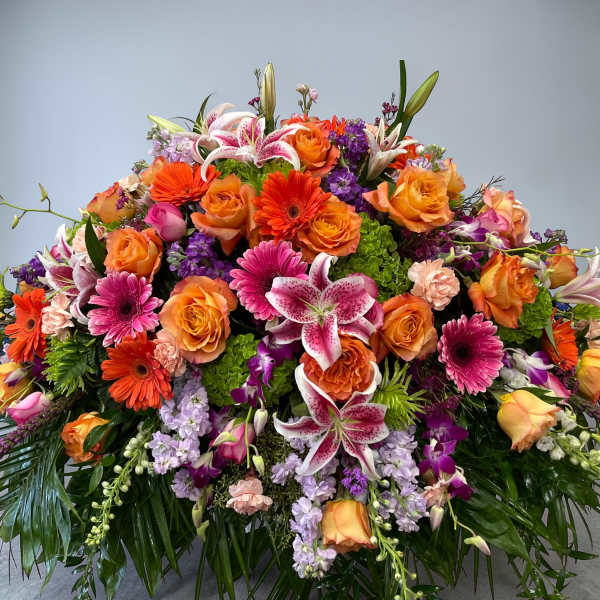 Large low arrangement of orange roses, pink lilies, gerbera daisies and purple flowers in a dome shape