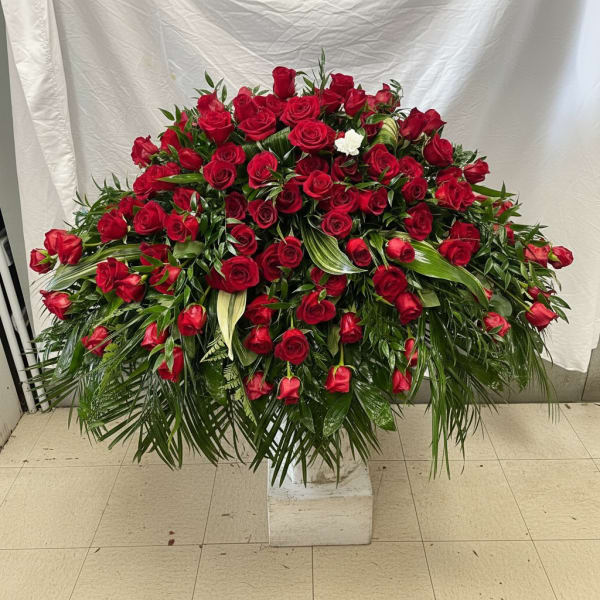 Large dome of red roses with one white flower and cascading palm fronds on a pedestal.