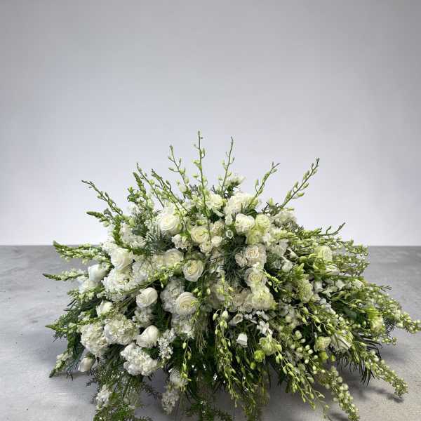 Low, elongated arrangement of white flowers with arching green buds in an all-around spray shape
