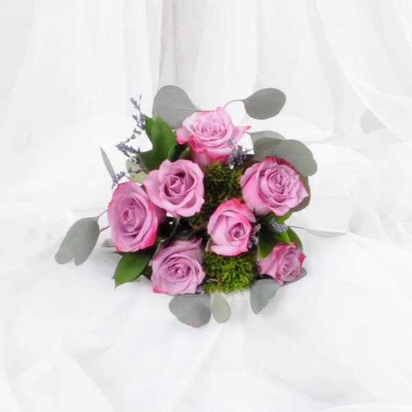 Round bouquet of pink roses with green moss accents resting on white fabric