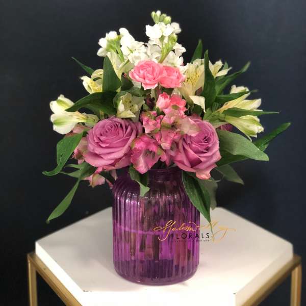 Pink and white flower arrangement in a purple glass vase