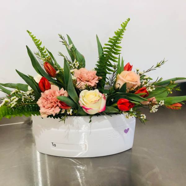 Mixed bouquet of roses, tulips, and carnations in a white container