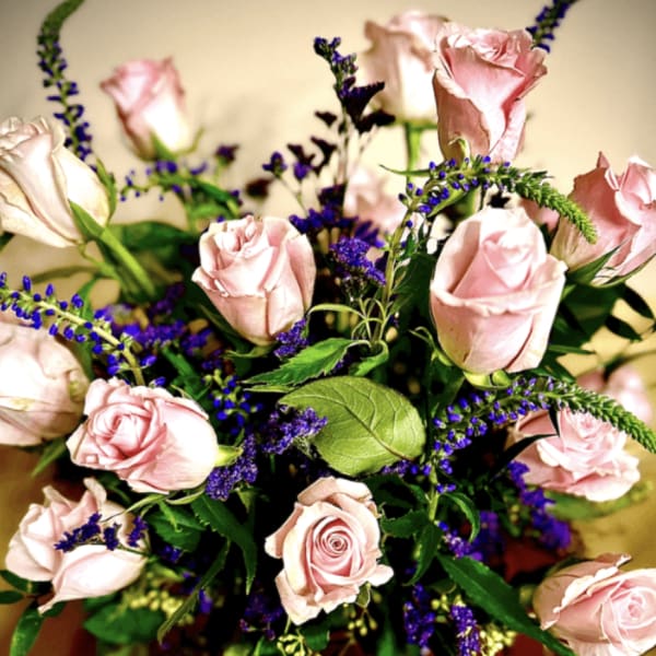 Bouquet of light pink roses with purple accent flowers in a clear vase