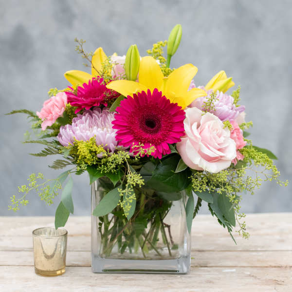 Pink and yellow mixed flower arrangement in a square glass vase