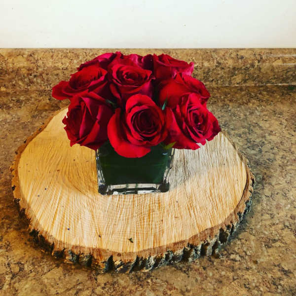 Red roses arranged in a square glass vase on a wood slice