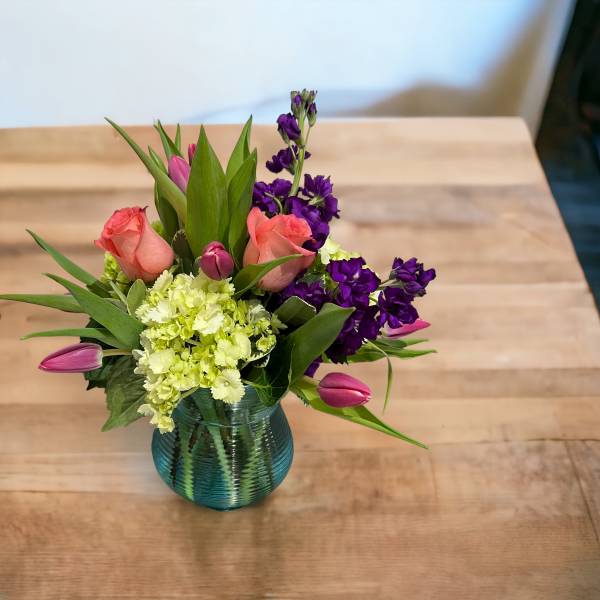 Pink roses and purple flowers arranged in a blue glass vase