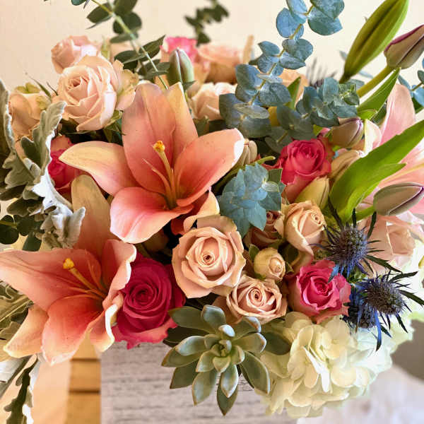 Bouquet of peach lilies, pink roses, and eucalyptus in a vase