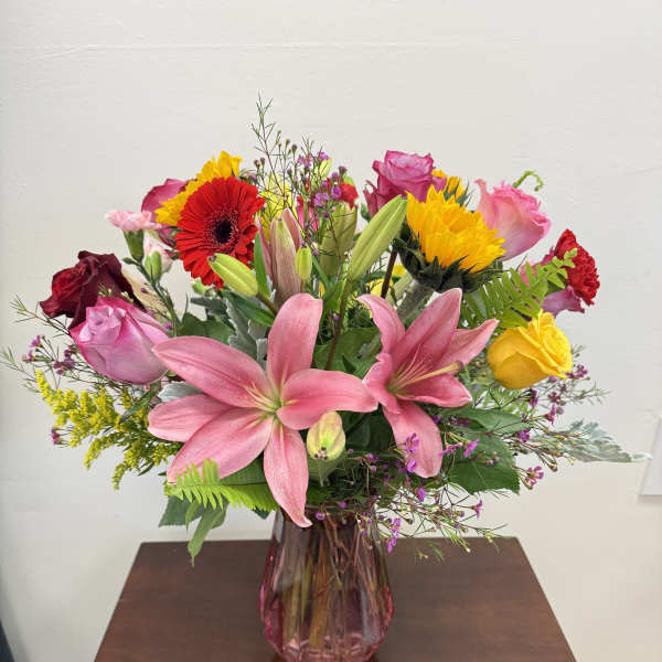 Mixed bouquet of pink lilies, roses, and bright gerbera daisies in a pink vase