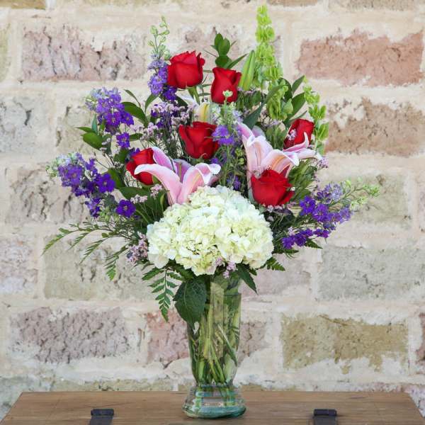 Bouquet of red roses, pink lilies, and white hydrangea in a glass vase