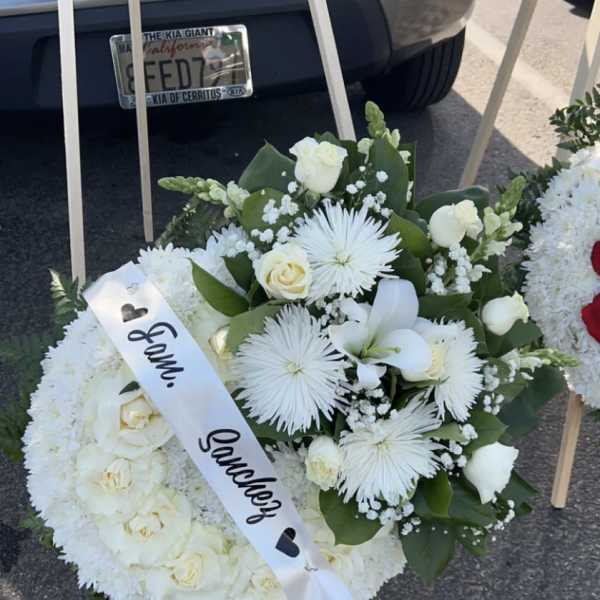 White funeral wreath with roses and a satin ribbon on an easel
