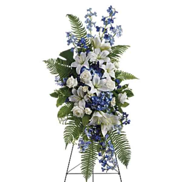 Standing floral spray with white lilies, roses, and blue flowers on an easel