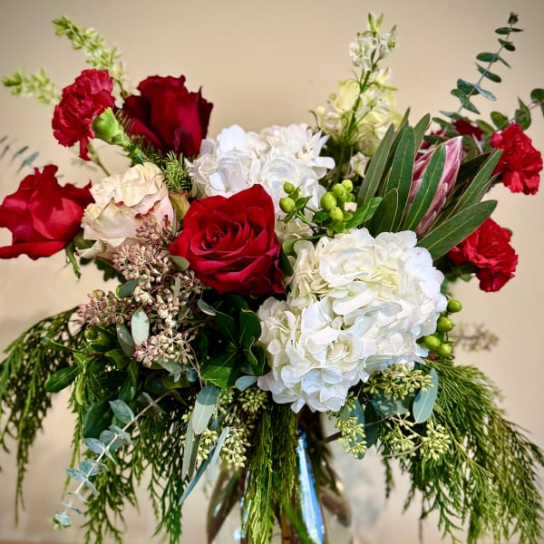 Tall arrangement of red roses, red carnations, white hydrangeas and evergreen foliage in a clear glass vase
